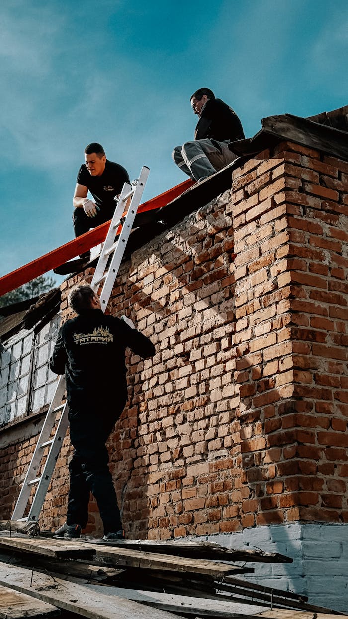 Three men repairing a brick wall outdoors on a sunny day. Teamwork and construction concept.